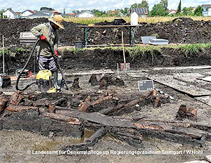 Mit dem Staubsauger im Einsatz: Ein Grabungsarbeiter bereitet die Reste des Holzbauwerks für die Fotodokumentation vor. (Quelle: W. Hohl, LAD)